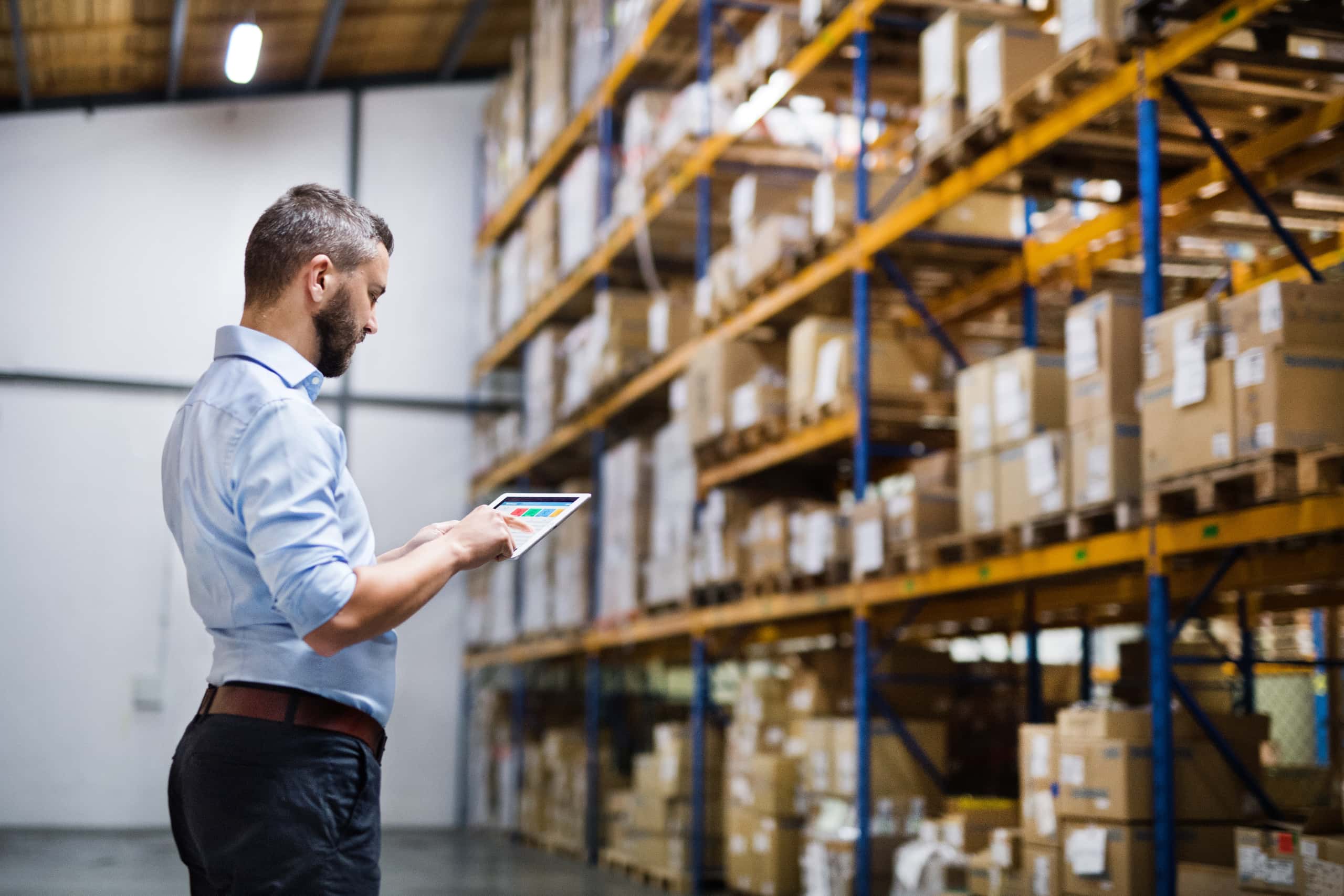manager-with-tablet Logpart - helhetslösning för tredjepartslogistik. I bild en man med en tablet. Mannen står fokuserad framför en stor lagerhylla.